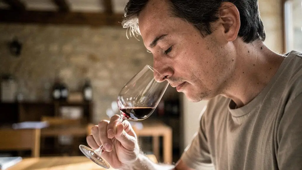 Dégustateur concentré humant un verre de vin pour analyser les arômes lors d'une dégustation à l'aveugle.